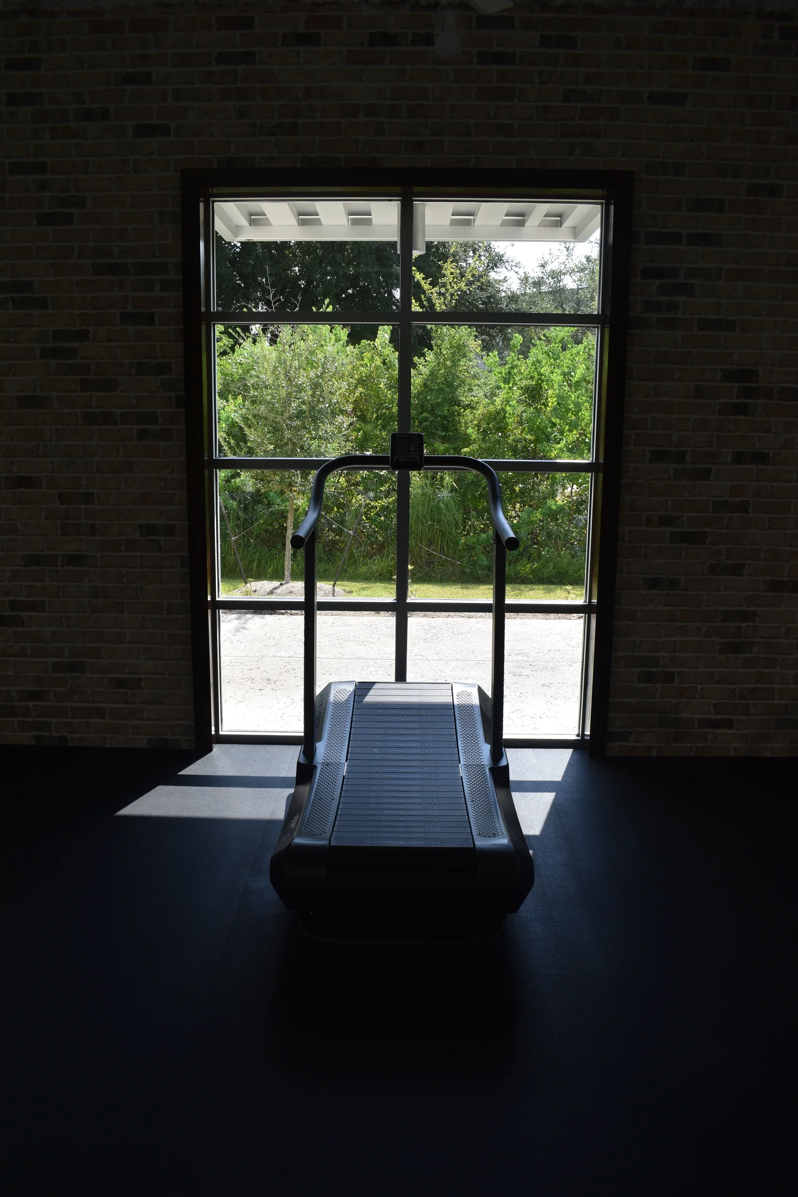 Commercial window set into exposed brick, with a treadmill inside and trees beyond the glass.